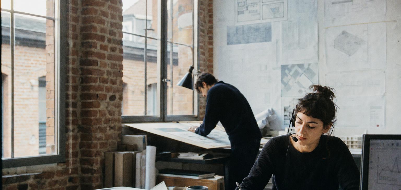 Dans un cabinet d’architectes, une jeune femme répond à un appel avec un casque en prenant des notes