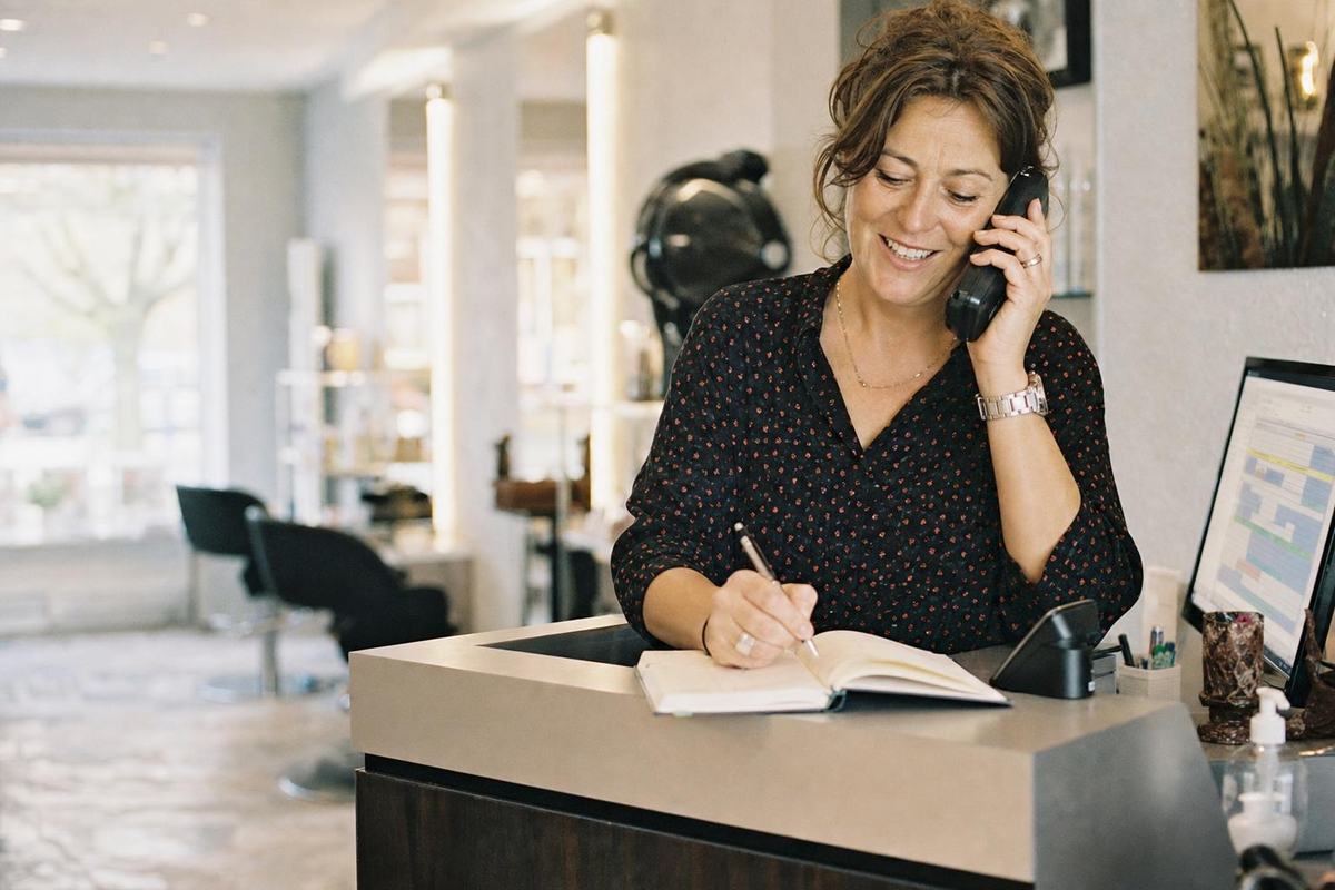 La gérante d’un salon de coiffure répond au téléphone derrière son comptoir en notant un rendez-vous